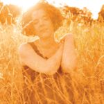 an artist in an orange dreamlike field in brandenburg closing her eyes in ecstasy